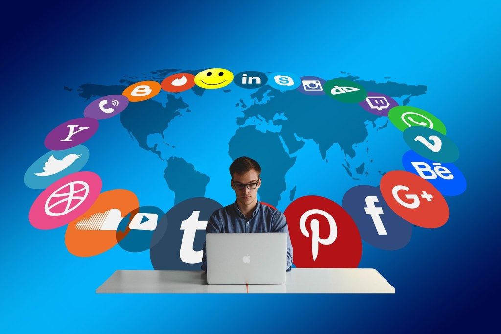 social media site logos behind a man sitting on his laptop